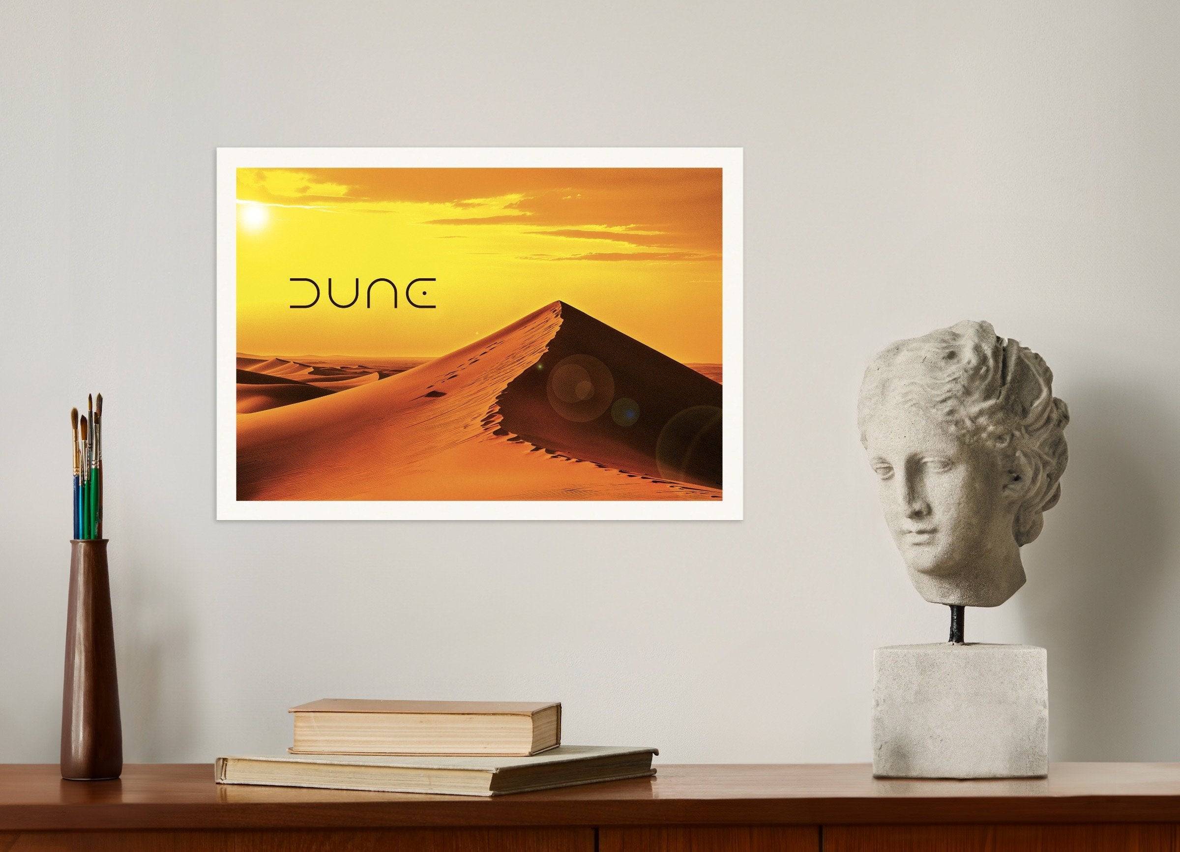Framed 'Dune' poster on a wall with a sculpture and books below.