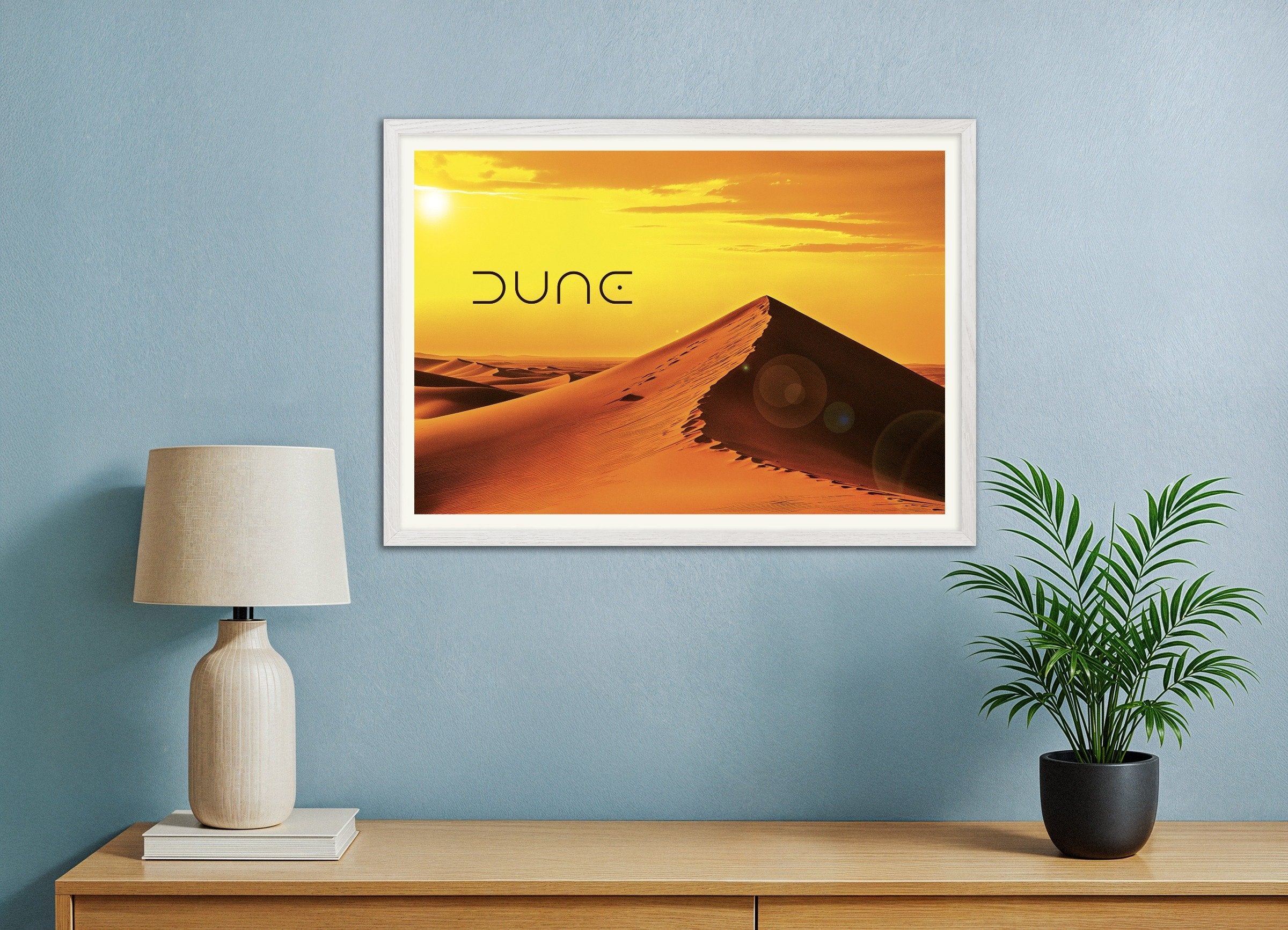 Framed artwork of a desert scene with 'Dune' text on a blue wall above a wooden shelf.
