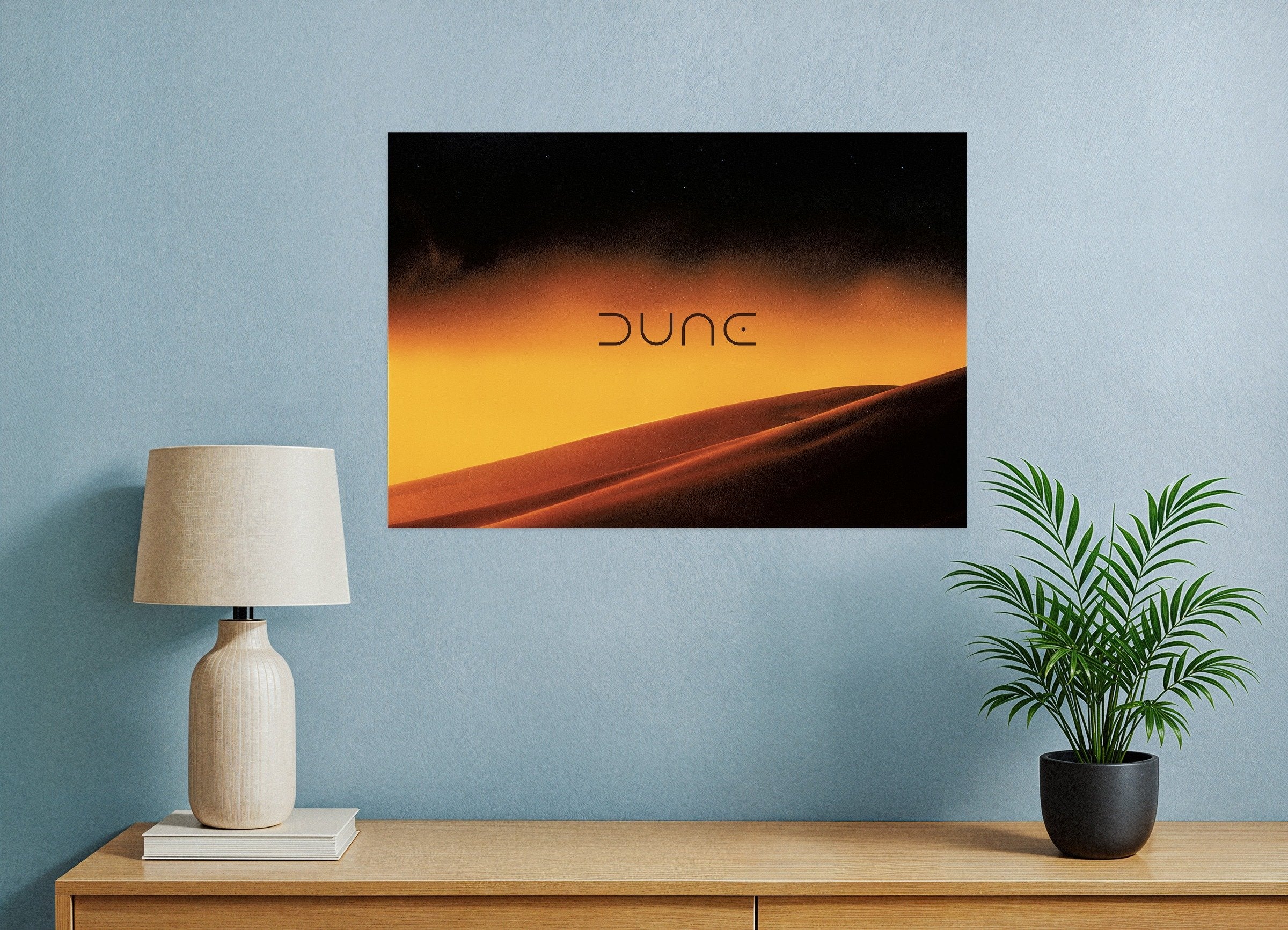 Wall art with 'Dune' title on a blue wall above a wooden shelf with a lamp and plant.