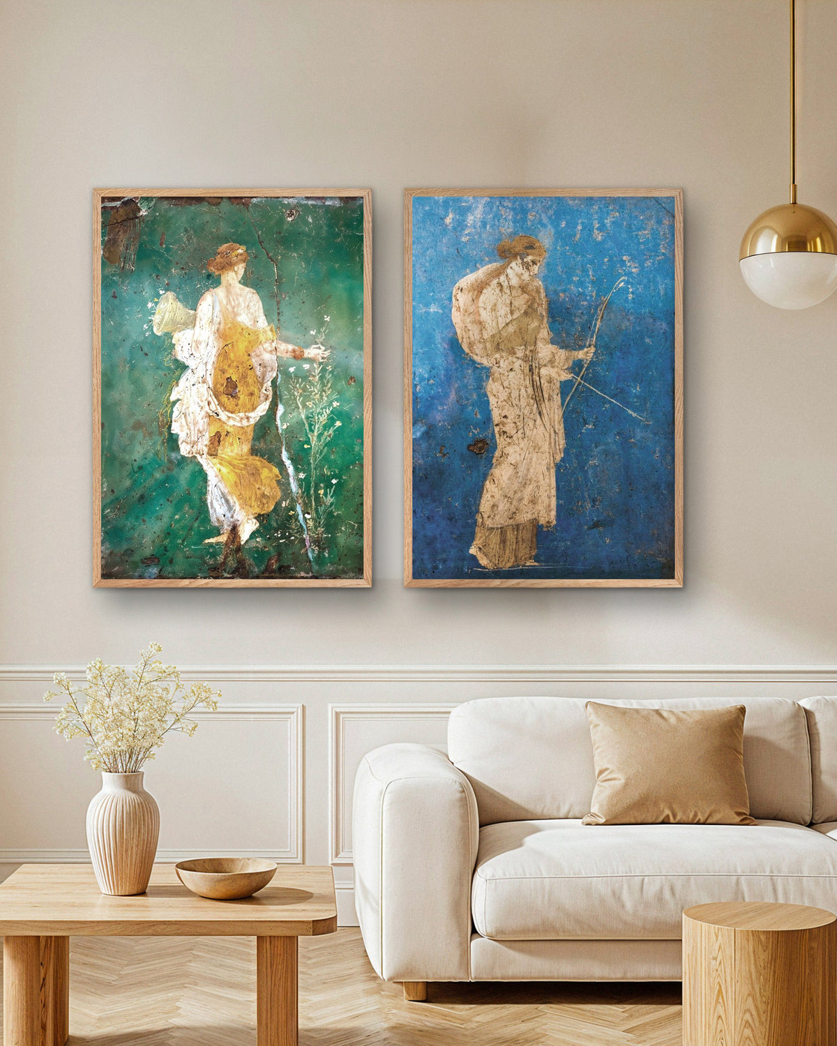 Set van 2 posters met Romeinse fresco’s, Flora en Artemis, in naturel houten lijsten boven een bank in een woonkamer
